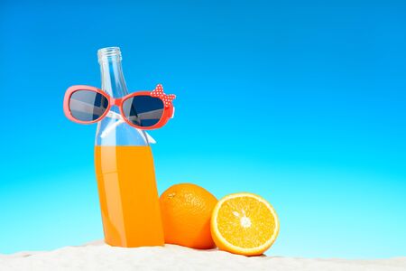 The bottle of orange juice and sunglasses on the beachの写真素材