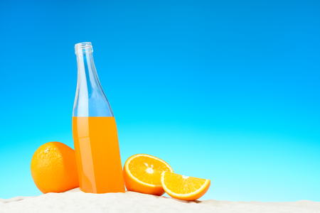 The bottle of orange juice and fruits on the beachの写真素材