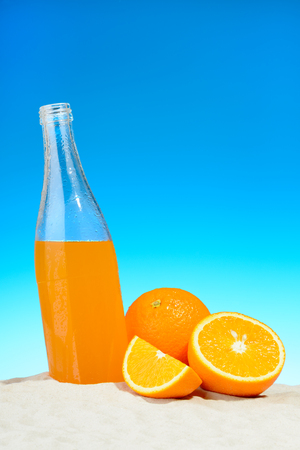 The bottle of orange juice and fruits on the beachの写真素材