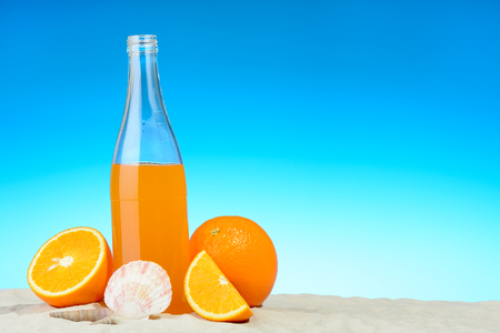 The bottle of orange juice and fruits on the beachの写真素材