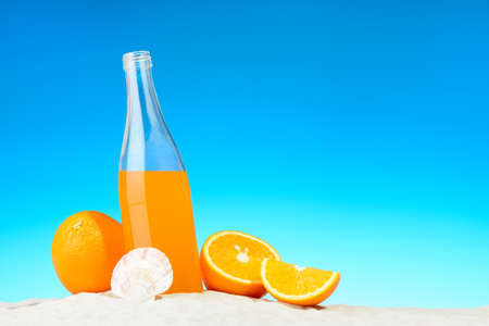 The bottle of orange juice and fruits on the beachの写真素材