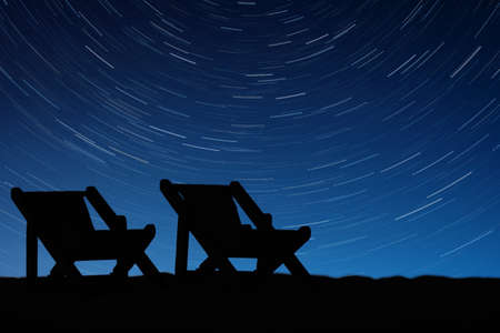 The silhouettes of the chairs on the background of star tracksの写真素材