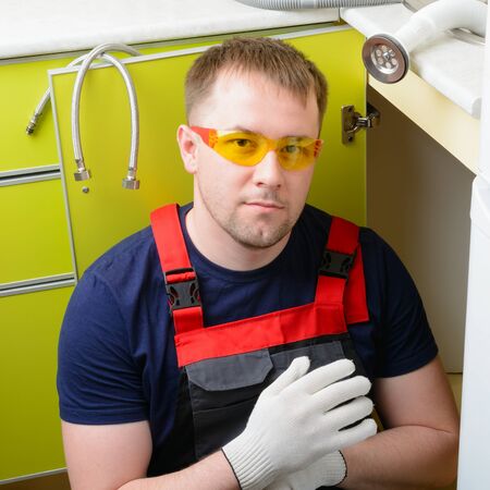 Plumber in the kitchen repairing the water pipe