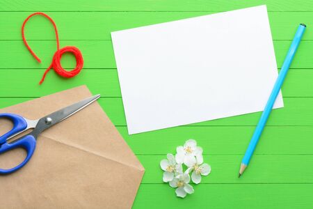 A blank piece of paper with an envelope on green wooden background