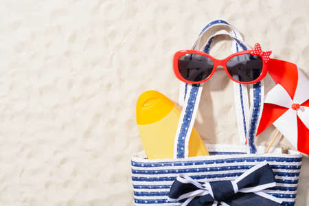 From above shot of bag with lotion, sunglasses and colorful pinwheel on sandの写真素材