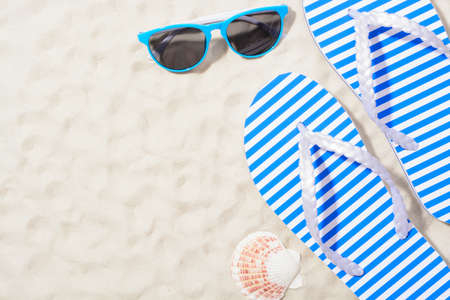 From above shot of striped flip flops on sand with sunglasses