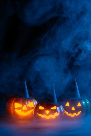 Three Halloween pumpkins with carved faces decorated with black witch hats glowing in smokeの写真素材