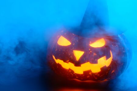 Composed glowing carved pumpkin in black witch hat lying on surface in mistの写真素材