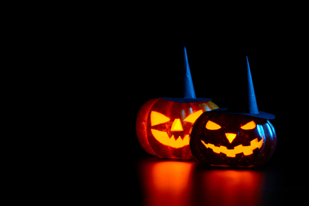 Two spooky carved pumpkins in black witch hats on table in darknessの写真素材