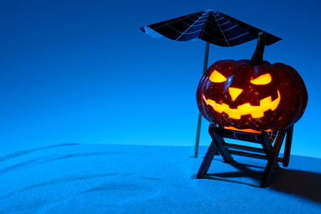 Glowing carved pumpkin on sunbed on beach in nighttimeの写真素材