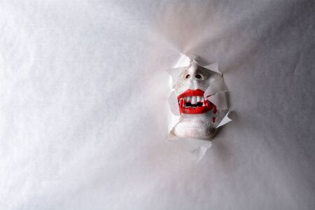 A horrifying vampire tearing a hole through paper revealing blood dripping fangs in a halloween horror theme.の写真素材