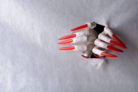 A horrifying vampire tearing a hole through paper with sharp red claws in a halloween horror themeの写真素材