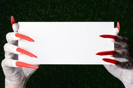 A scary halloween vampire with sharp claws holding a blank card with copy space.の写真素材