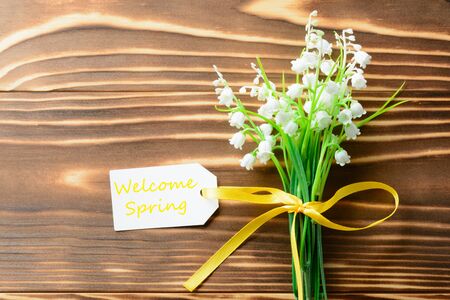 From above small bunch of white flowers and welcome spring label on wooden tableの写真素材
