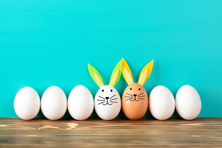 Chicken eggs arranged in row with two being decorated with bunny ears and snoutsの写真素材