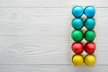 Colorful easter eggs in a tray on a white wooden background. Top viewの写真素材