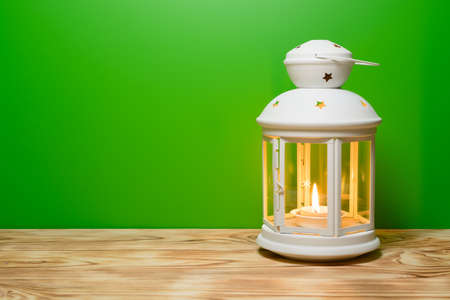 A lantern with a glowing candle in on the wooden table, green backgroundの写真素材