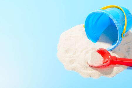 Toy plastic bucket and shovel in the sand. Blue background with copy spaceの写真素材
