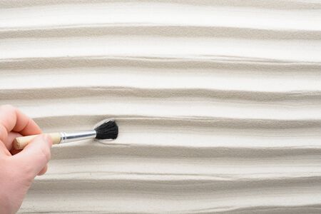 Men's hand draws brush patterns on sand