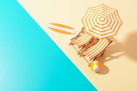 Flat lay of a composed miniature of beach lounge area with umbrella and sunbeds on the colorful surface.の写真素材