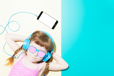 From above of girl with braids in swimwear and sunglasses listening to music with headphones and phone on colorful background. の写真素材
