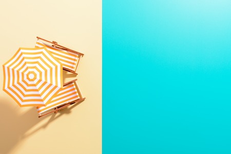 Flat lay of a composed miniature of beach lounge area with umbrella and sunbeds on the colorful...