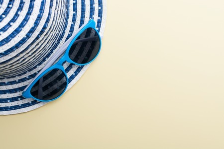 Top view of a hat and blue sunglasses on a beige surfaceの写真素材