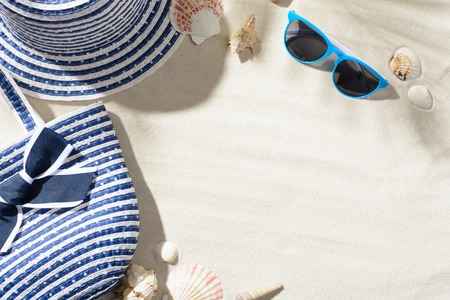 Beach hat, sunglasses, and bag are among the seashells on the sandの写真素材