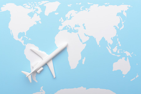 Top view of miniature plane placed on top of blue and white colored map of worldの写真素材