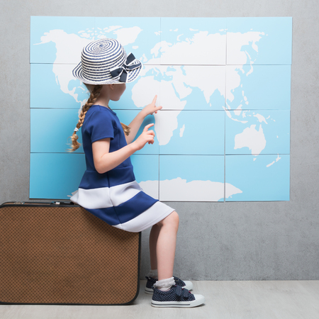 Little girl in summer hat sitting back on luggage and touching countries on Earth modelの写真素材