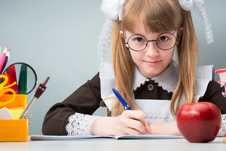 Female child in glasses with tails sitting at table with apple and writing in copybookの写真素材