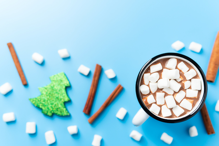 From above shot of metal cup with cacao and marshmallows on the blue background with cinnamon sticksの写真素材