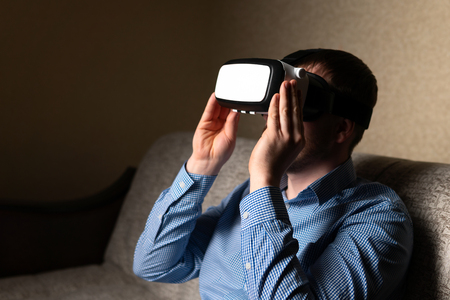 Unrecognizable adult male wearing modern VR headset while sitting on comfortable sofa at homeの写真素材
