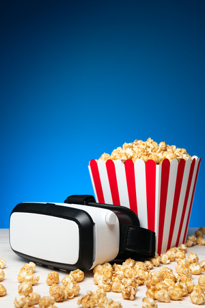 Arrangement of crispy golden popcorn in striped bucket and glasses of virtual reality on blue backgroundの写真素材