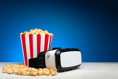 Arrangement of crispy golden popcorn in striped bucket and glasses of virtual reality on blue backgroundの写真素材