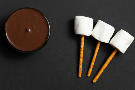 Top view of melted chocolate in a bowl with white fluffy marshmallows on sticksの写真素材