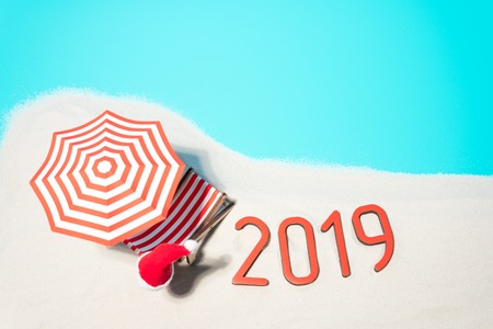 From above of layout of sunshades and Santa hats on cartoon beach with congratulations of 2019 New...