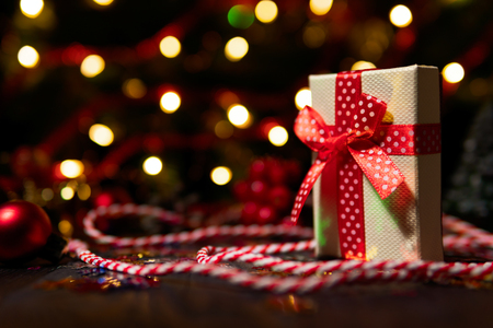 Box in red ribbon composed on wood table with colorful string and glowing garland lightsの写真素材