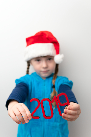Closeup of red number 2019 in hands of little girl wearing Santa hat on white background