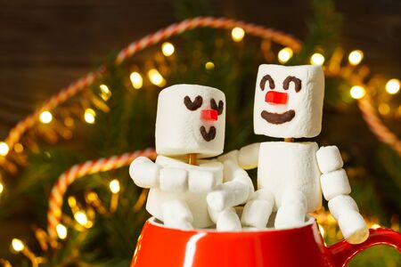 Red mug with hot chocolate and two snowmen in love made from marshmallows. Christmas and New Year composition.の写真素材