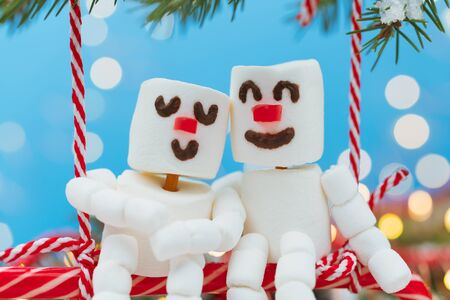 Two lovers of Marshmallow snowmen are sitting on a swing of candy. Christmas meeting a couple in love concept.の写真素材