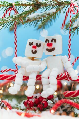 Two lovers of Marshmallow snowmen are sitting on a swing of candy. Christmas meeting a couple in love concept.の写真素材