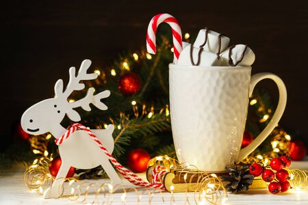 Sweet marshmallows and candy in a white ceramic mug on a miniature sleigh with a harnessed toy deer. Festive composition with Christmas and New Year decorations.の写真素材