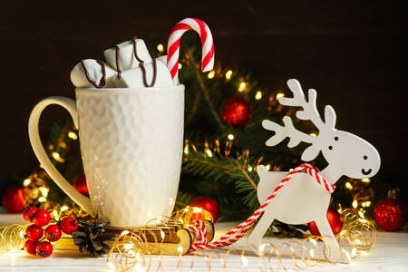 Sweet marshmallows and candy in a white ceramic mug on a miniature sleigh with a harnessed toy deer. Festive composition with Christmas and New Year decorations.の写真素材