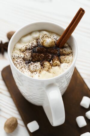 White mug with hot chocolate and marshmallows with cinnamon stick on a wooden table. Hot winter drink, top view.の写真素材