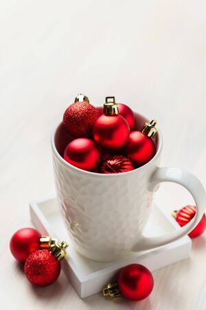 Red Christmas decorative balls in a white mug. White wooden table top view with blank space.の写真素材