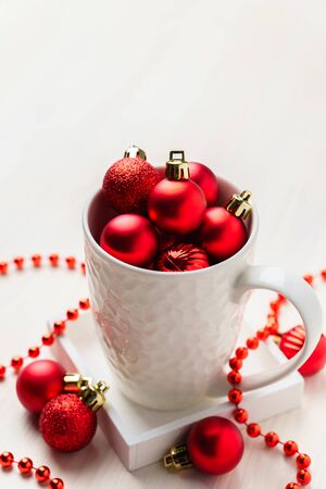 Red Christmas decorative balls in a white mug. White wooden table top view with blank space.の写真素材
