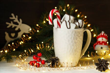 Sweet marshmallows and candy in a white ceramic mug on a wooden table with Christmas and New Year decorations. Festive composition.の写真素材