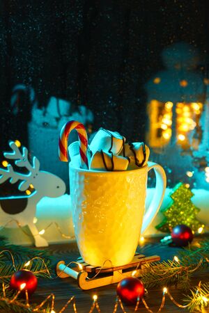 White mug with hot chocolate and marshmallows with Christmas decorations on the windowsill on a winter evening at the blue window.の写真素材