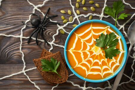 A healthy pumpkin puree garnished with cream and parsley leaves. Composition autumn cream soup with toys for the holiday Halloween on a dark wooden background, top view.の写真素材